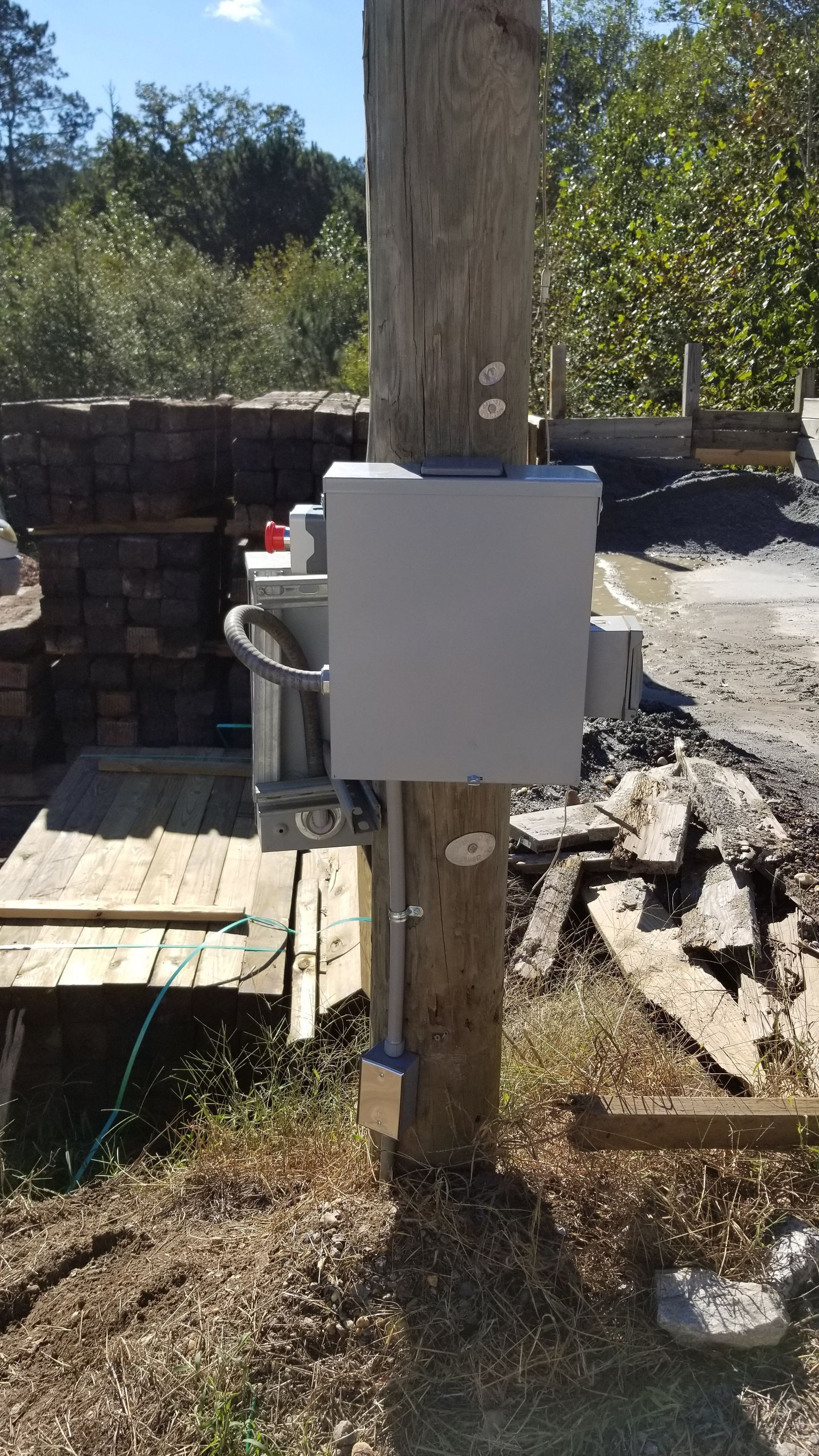 Electrical boxes and conduit mounted on a weathered utility pole outdoors.