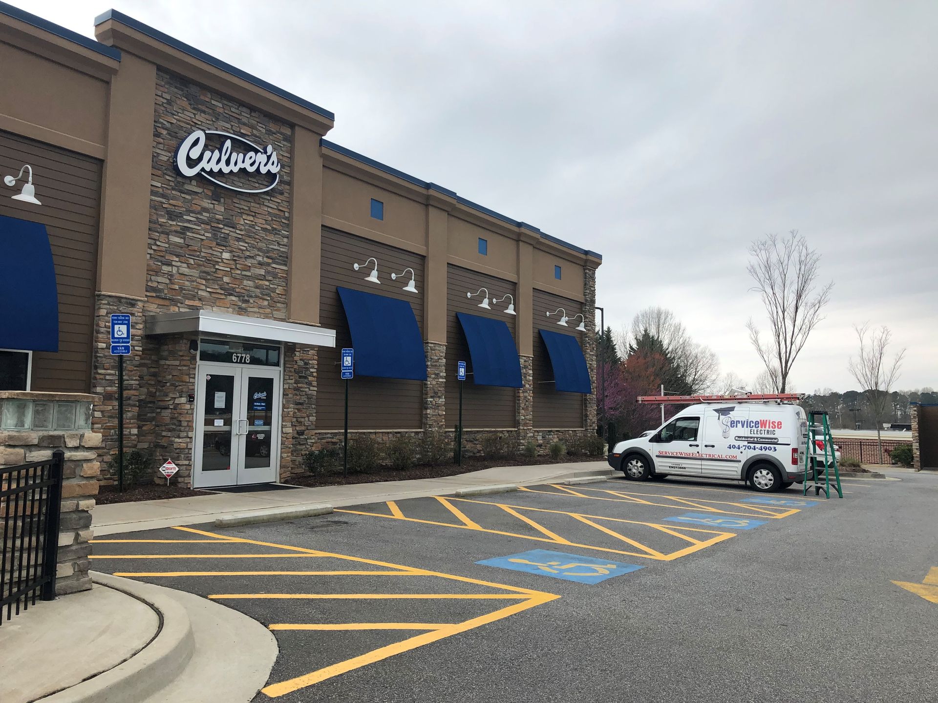 Culver's restaurant exterior with a white service van parked nearby. Blue awnings, accessible parking spaces, and cloudy sky.