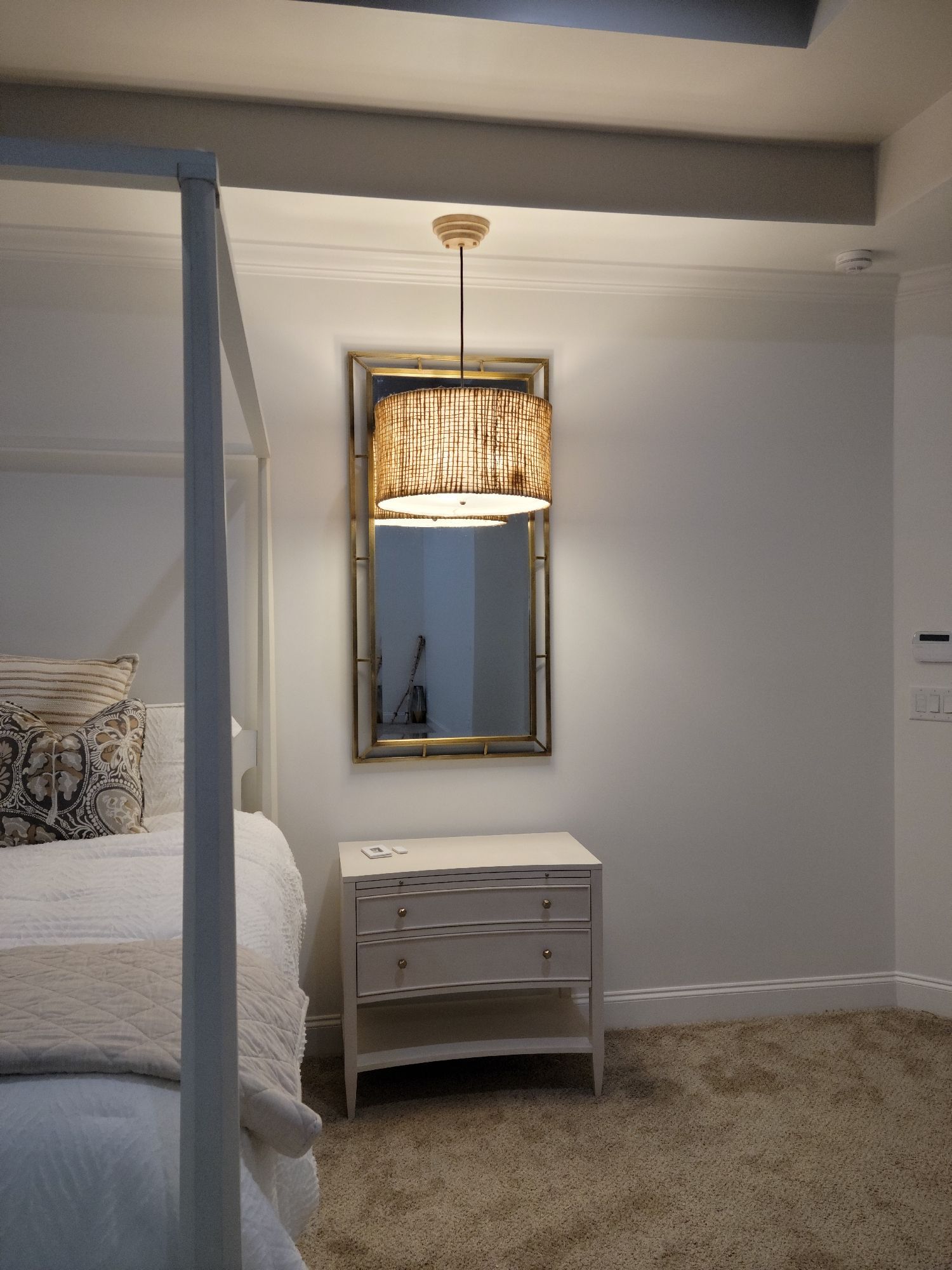 Bedroom with canopy bed, nightstand, mirror, and pendant light.
