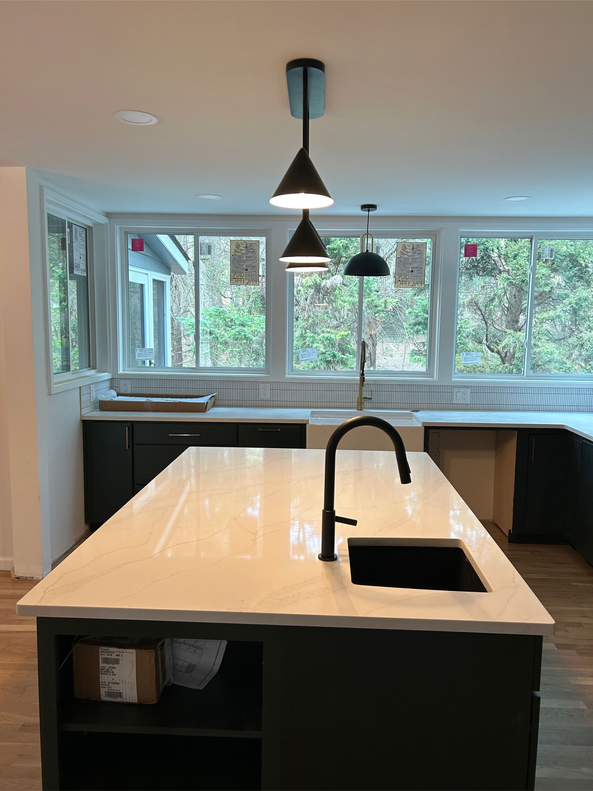 Kitchen island with white countertop, black cabinets, black faucet, and pendant lights.