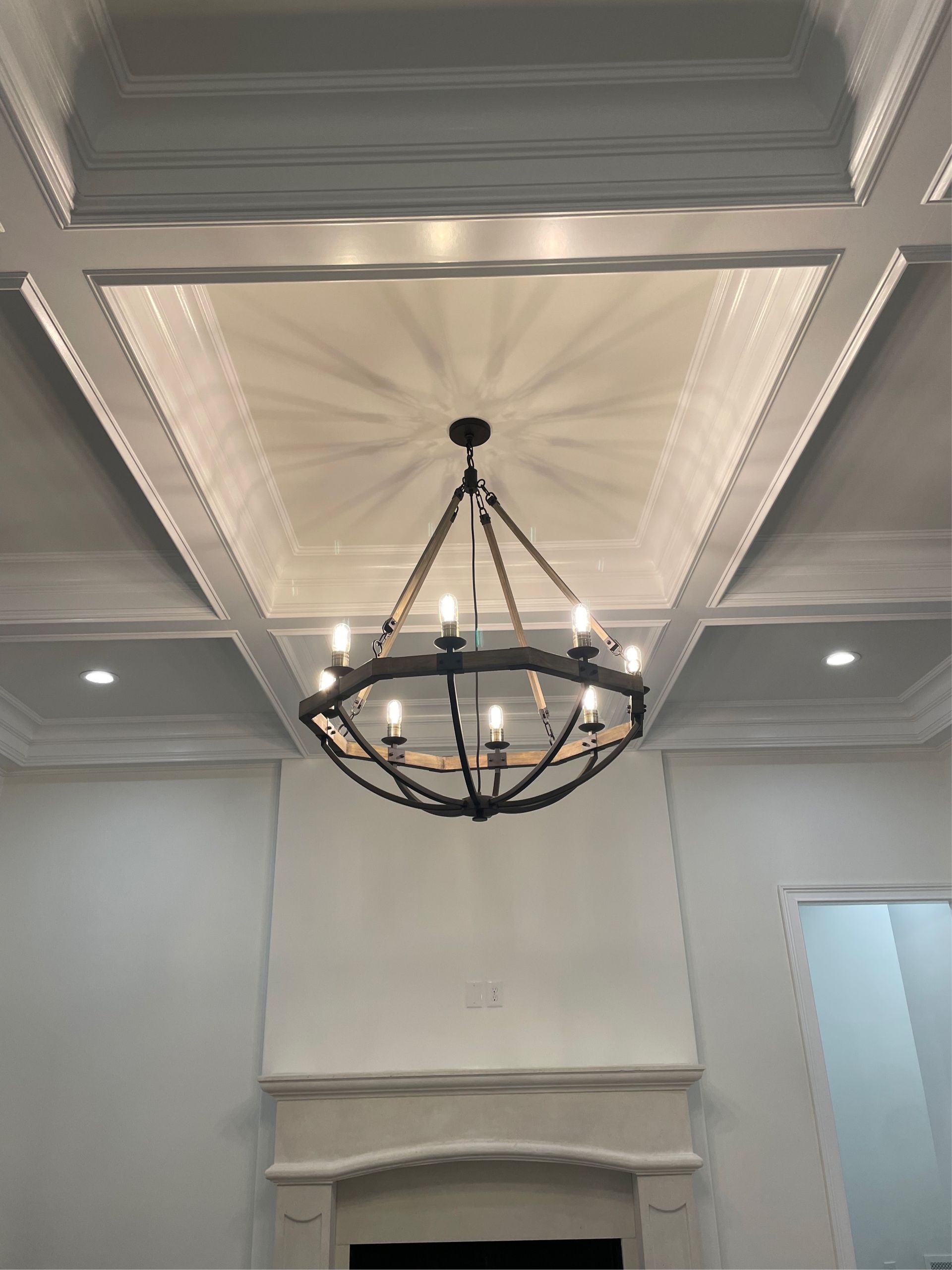Chandelier hanging from a coffered ceiling, above a fireplace, white walls.