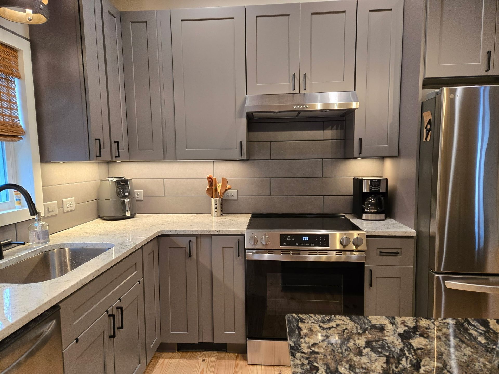 Gray kitchen cabinets with stainless steel appliances, white countertops, and a subway tile backsplash.