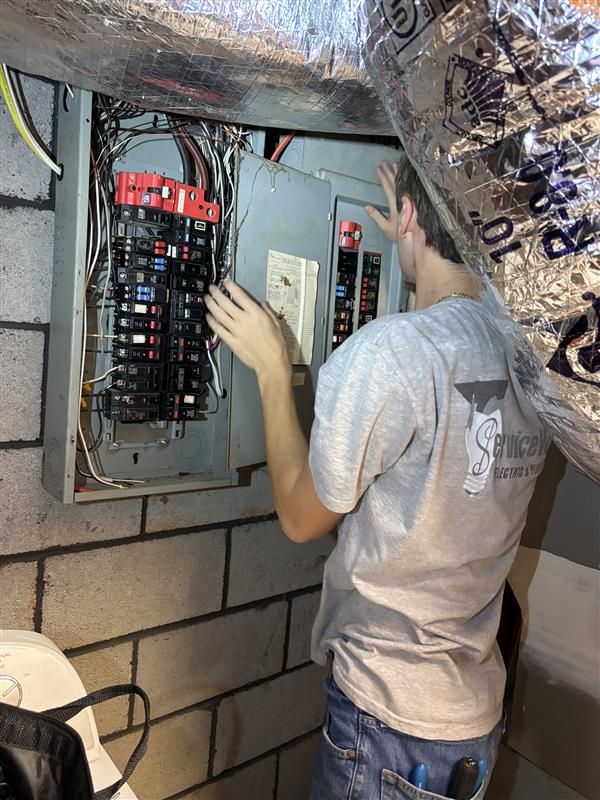 Electrician working on an electrical panel in a brick-walled basement.