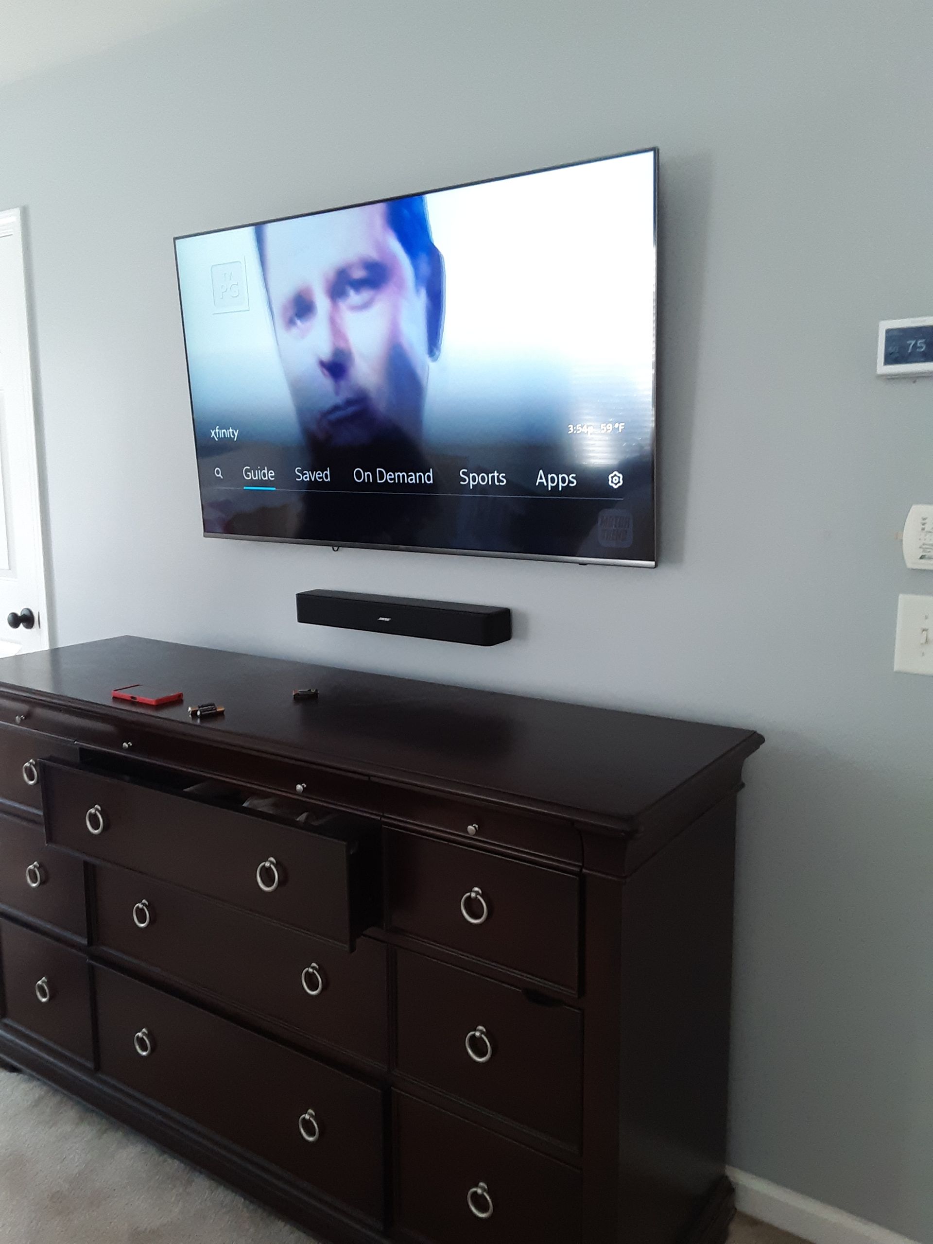 A TV mounted above a dark dresser with a soundbar. The wall is light gray.