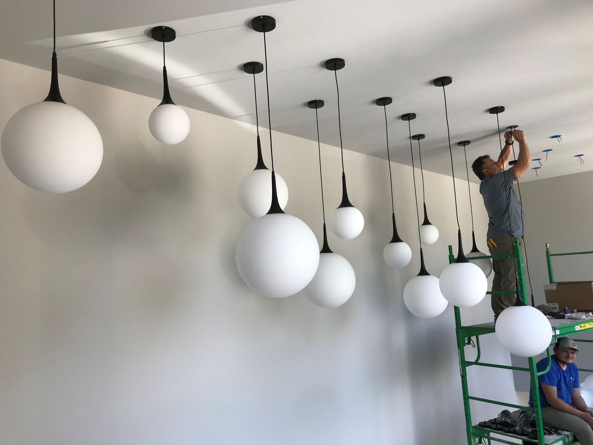Person installing pendant lights on a ceiling. White globe lights hang from black cords.