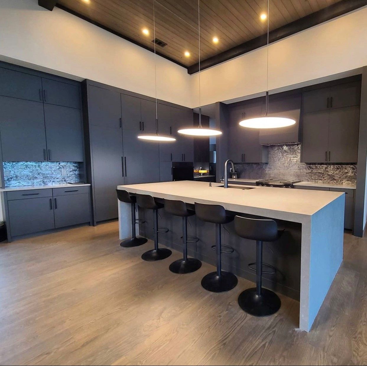 Modern kitchen with gray cabinets, large island with stools, and pendant lights.
