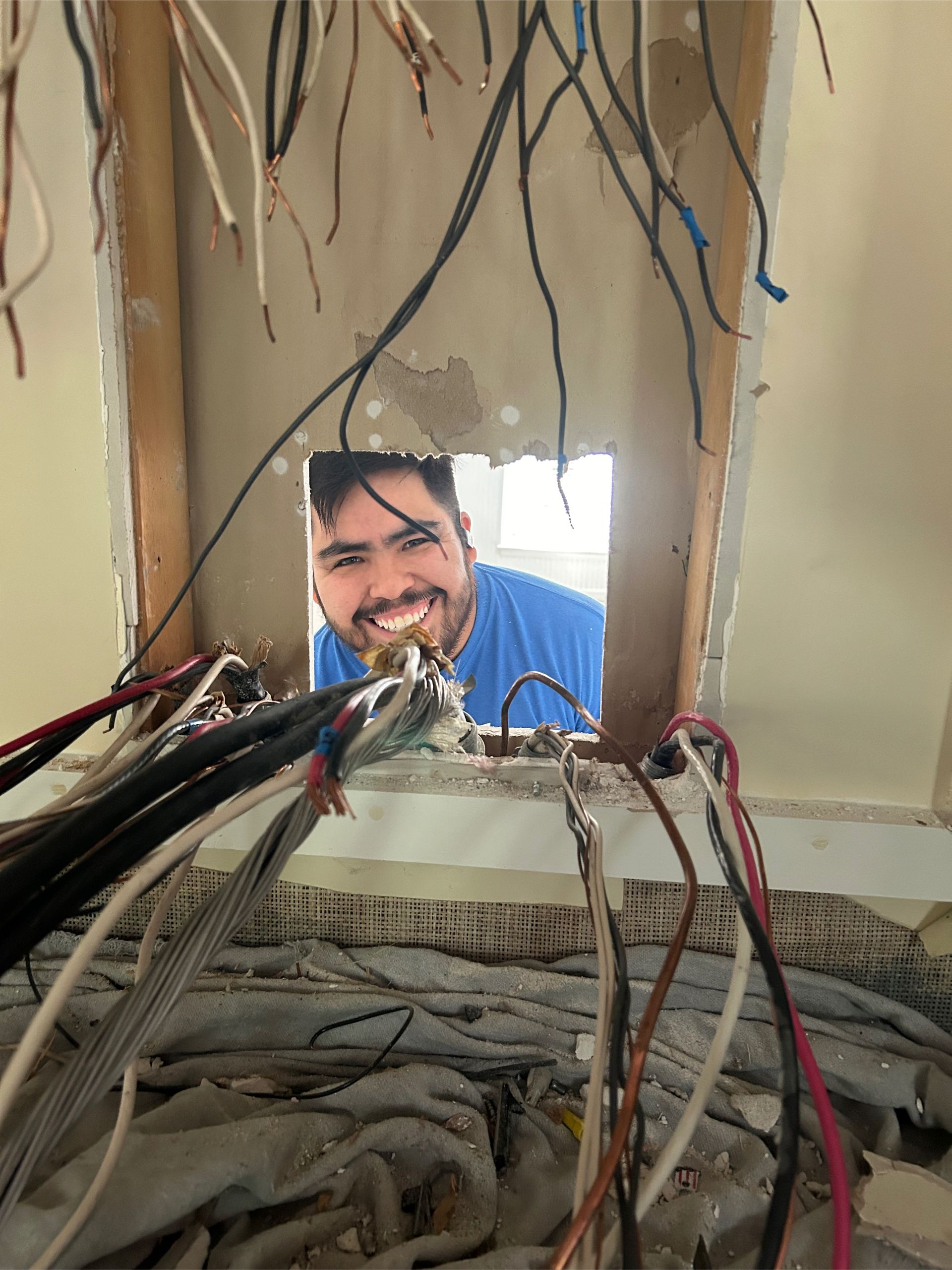 Man smiling through a hole in a wall, surrounded by exposed wires.
