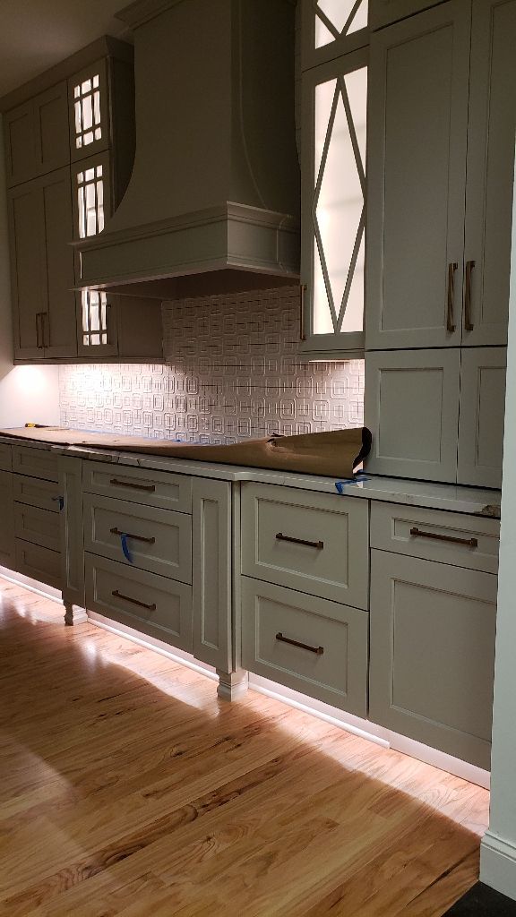 Kitchen with light gray cabinets, wood floors, and backsplash; under-cabinet lighting.