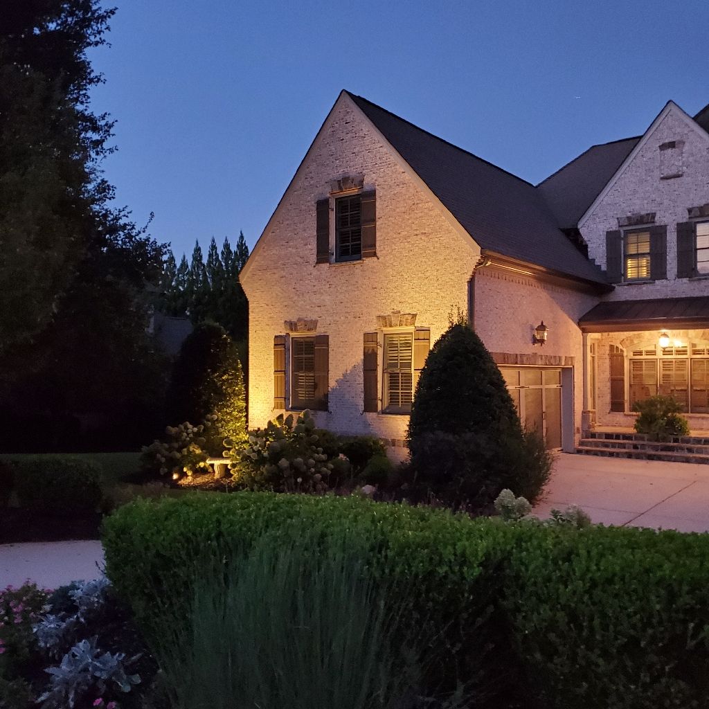 Night view of a two-story brick house with lit windows and landscaping; blue sky background.