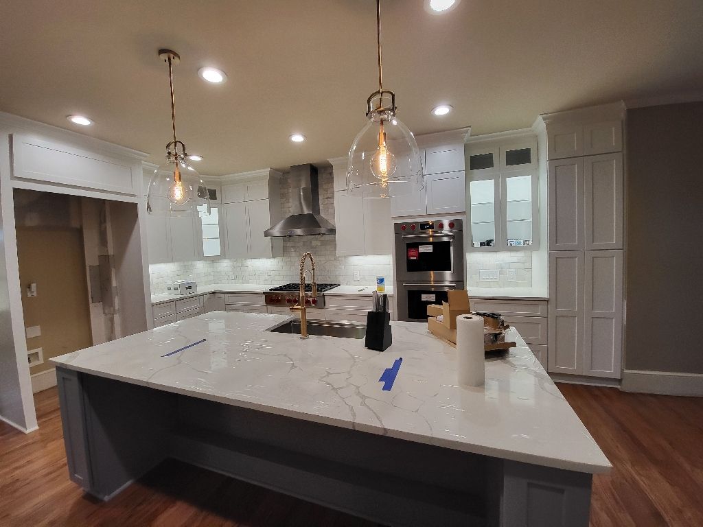 Spacious kitchen with large island, stainless steel appliances, and hanging lights.
