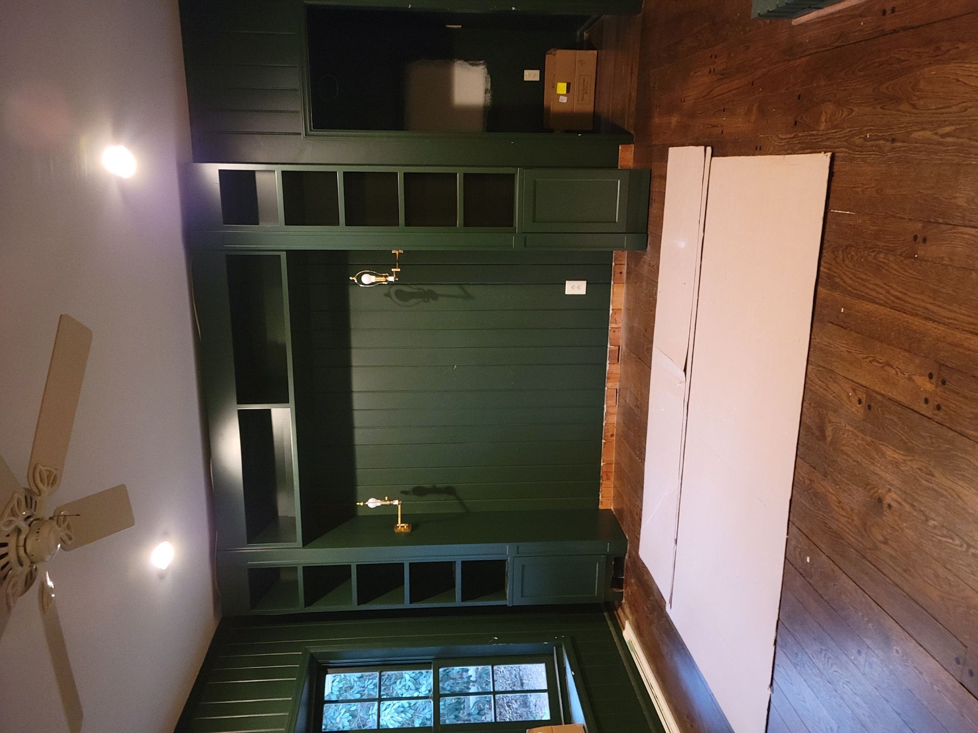 Green built-in shelving and cabinets on a wall, with white panels and hardwood floors.