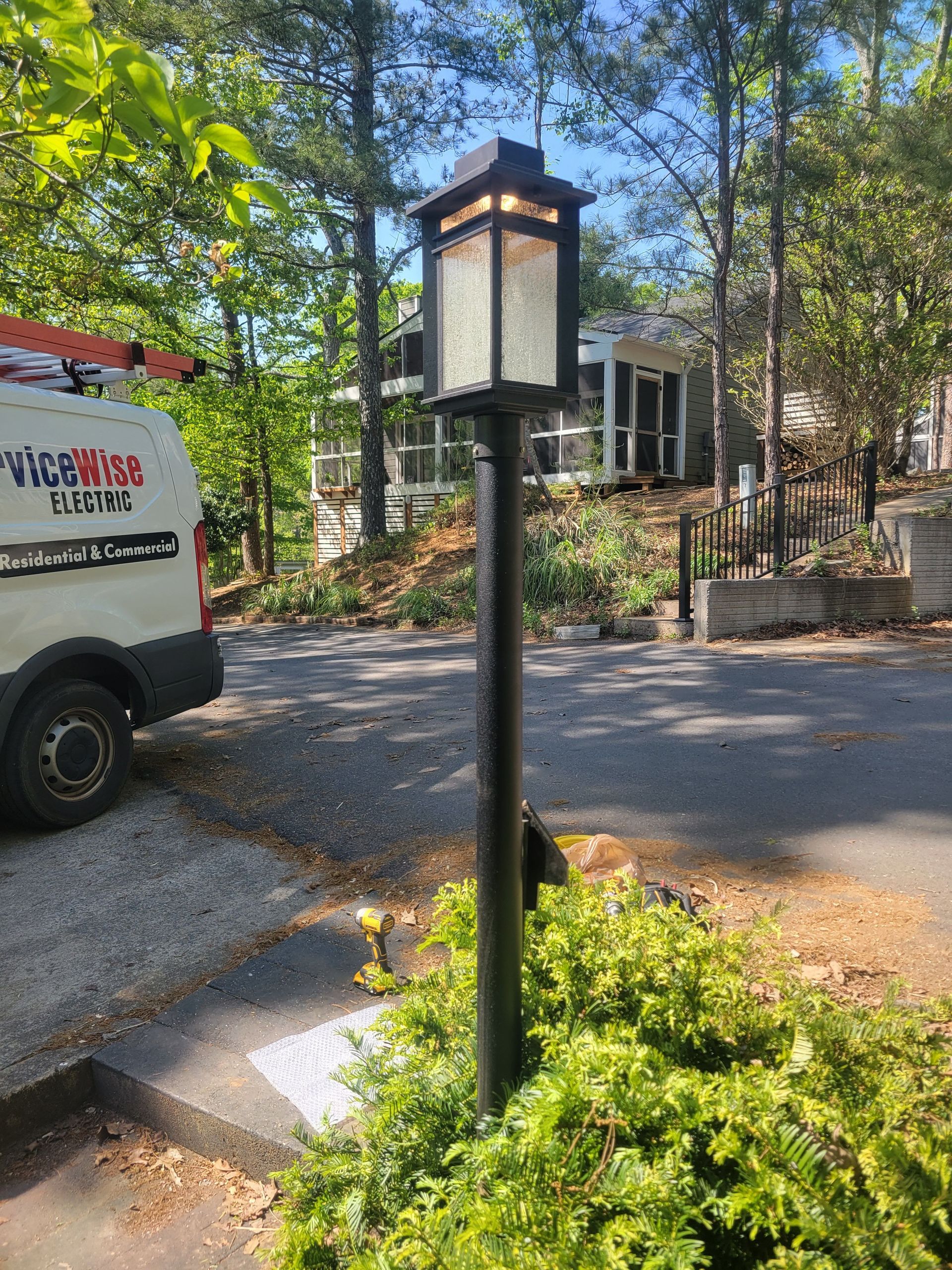Black lamp post with a decorative light fixture, in a yard, near a van.