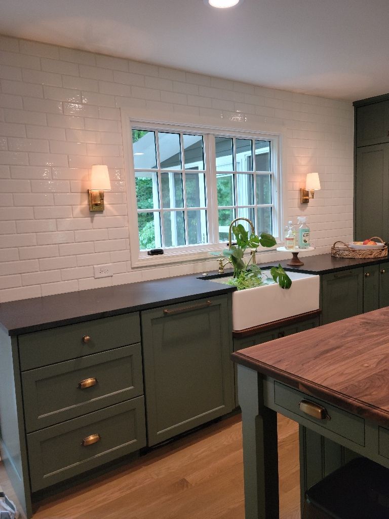 Green kitchen with white tile backsplash, a window, and dark countertops.