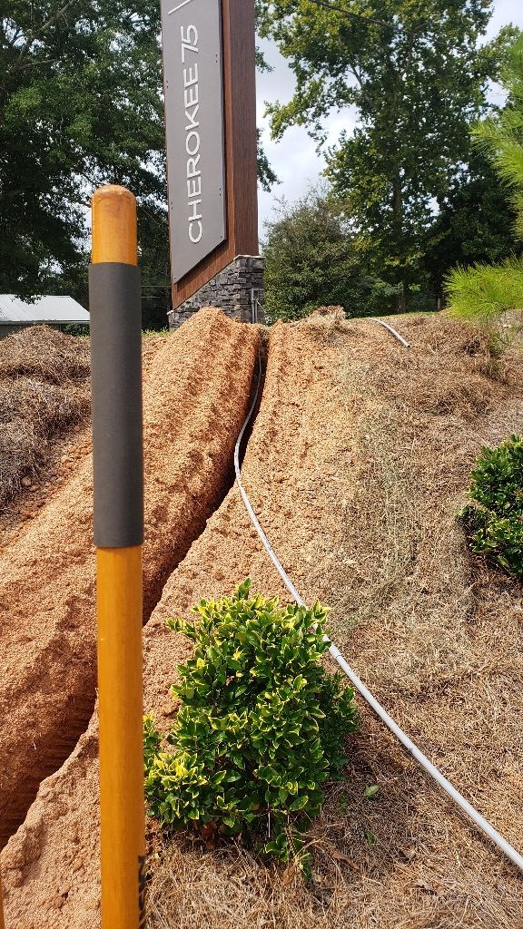 Sign next to a hillside trench with a utility pole and a bush, wood chip ground cover.