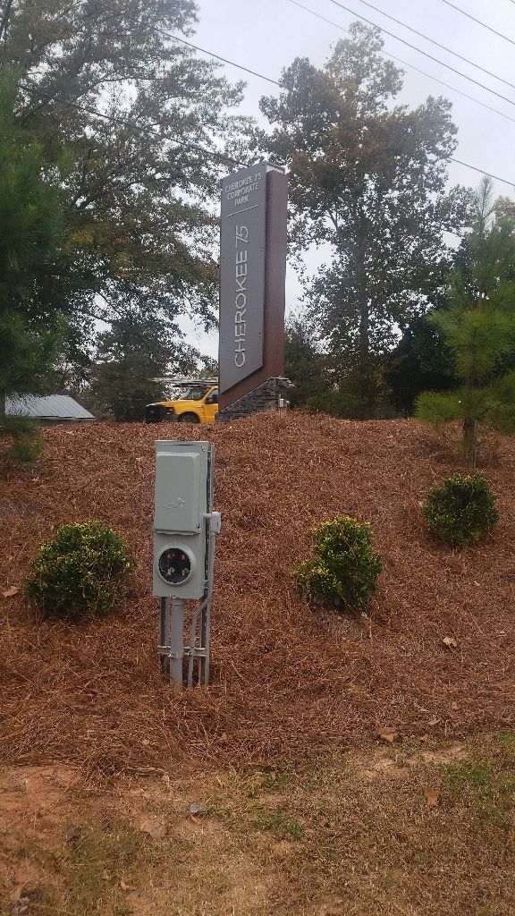 Monument sign with text, on a bed of mulch, with electrical box in foreground.