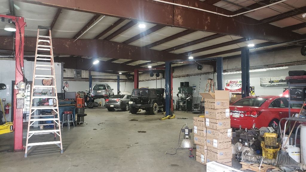 Inside auto repair shop with vehicles on lifts, tools, and a ladder.