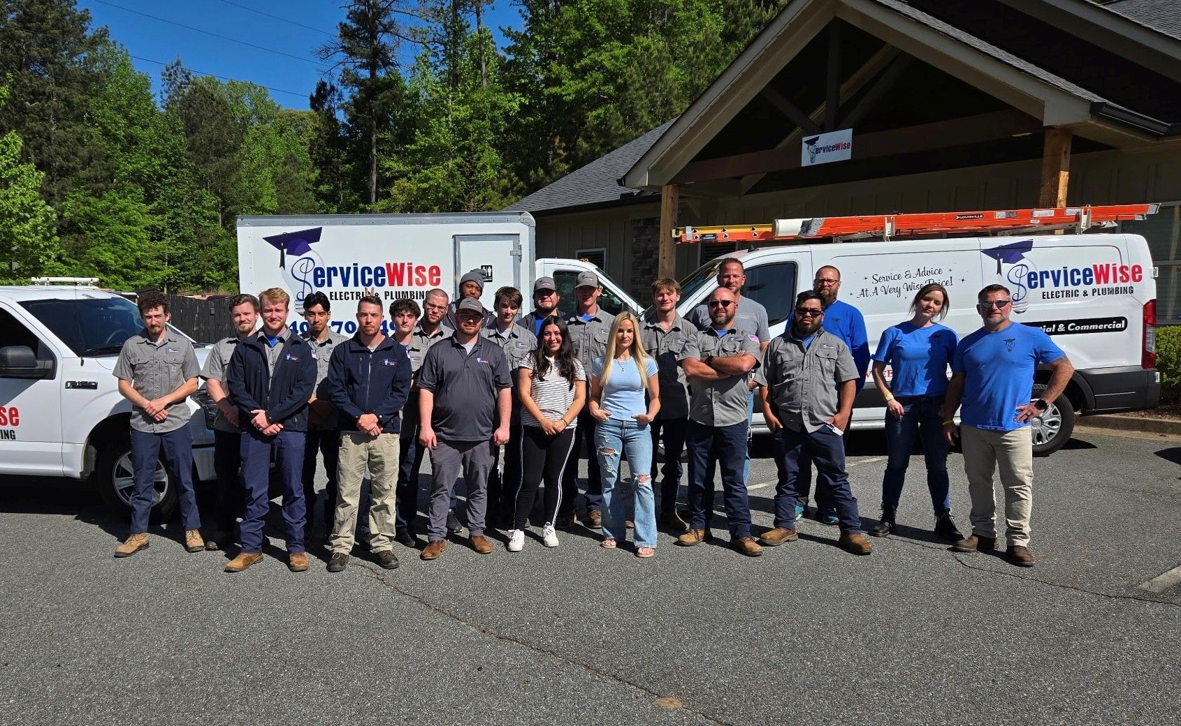 Group of people wearing blue jackets posing near a white truck and vans.