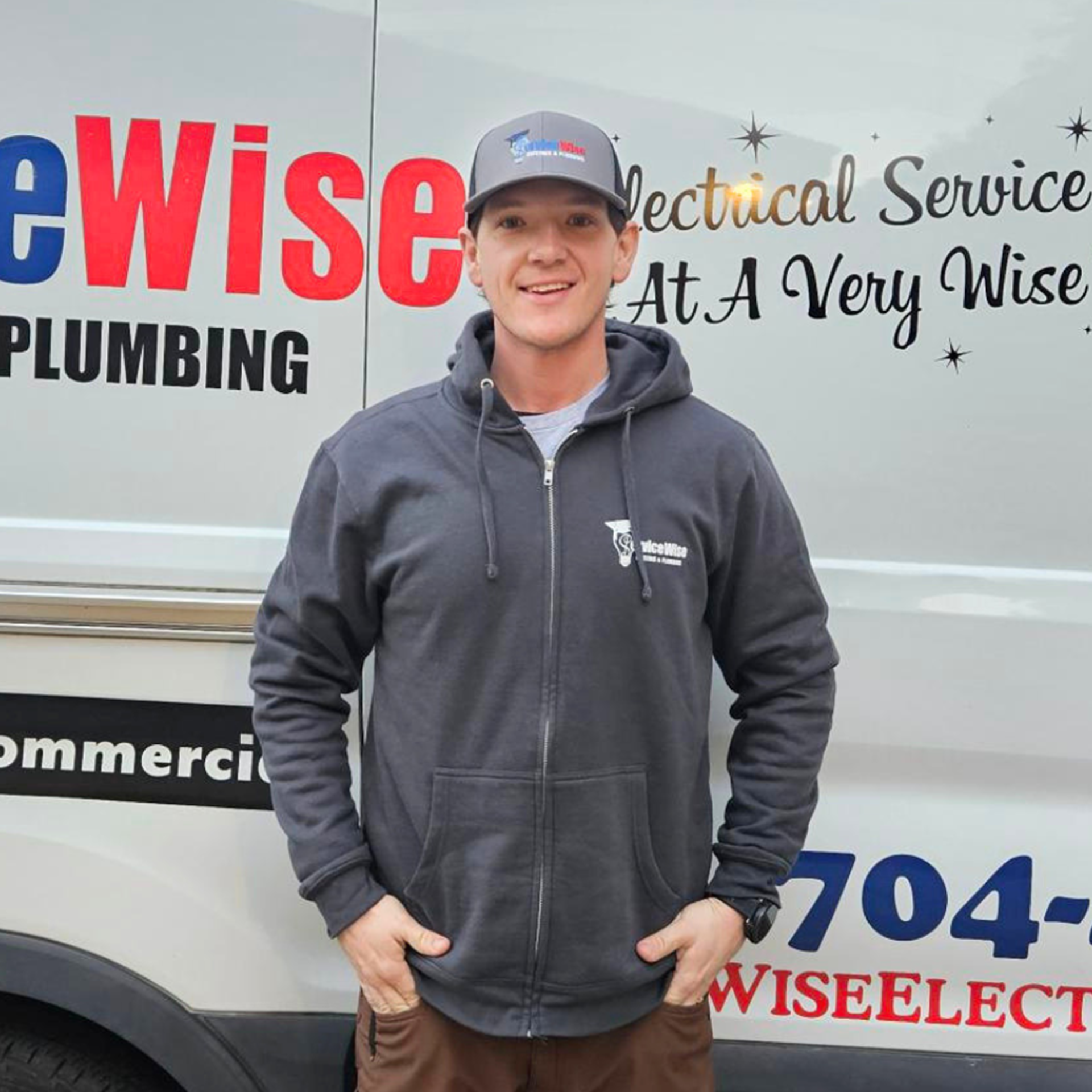 Man in navy jacket and cap stands next to a white van with red 