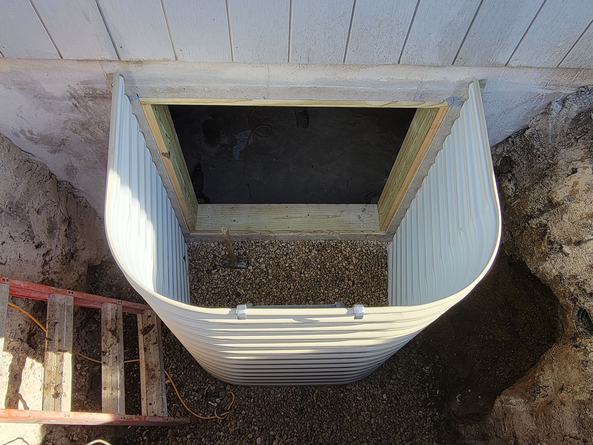 A ladder is sitting next to a window well in a basement.