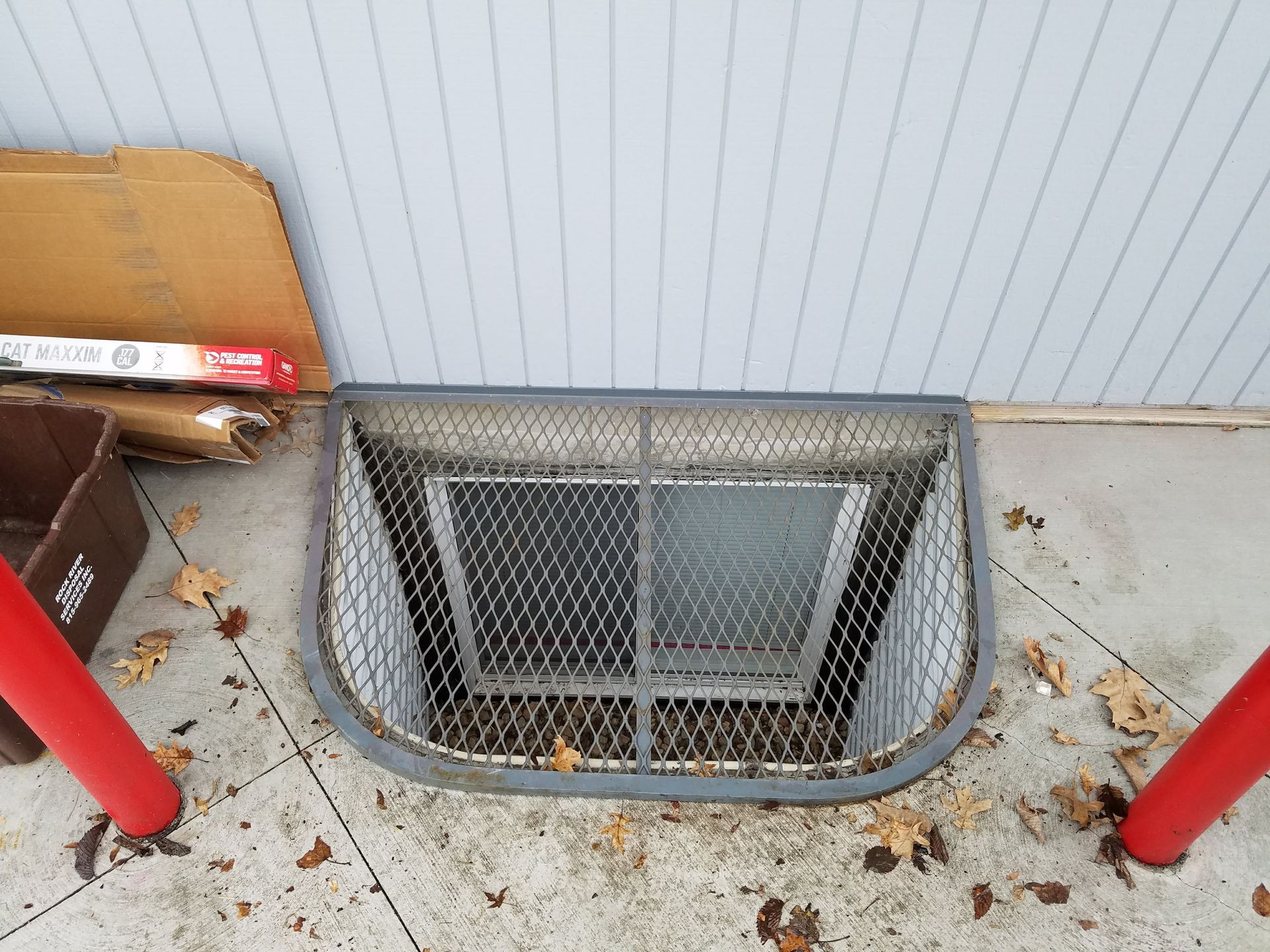 A window well with a metal grille on the side of a building.