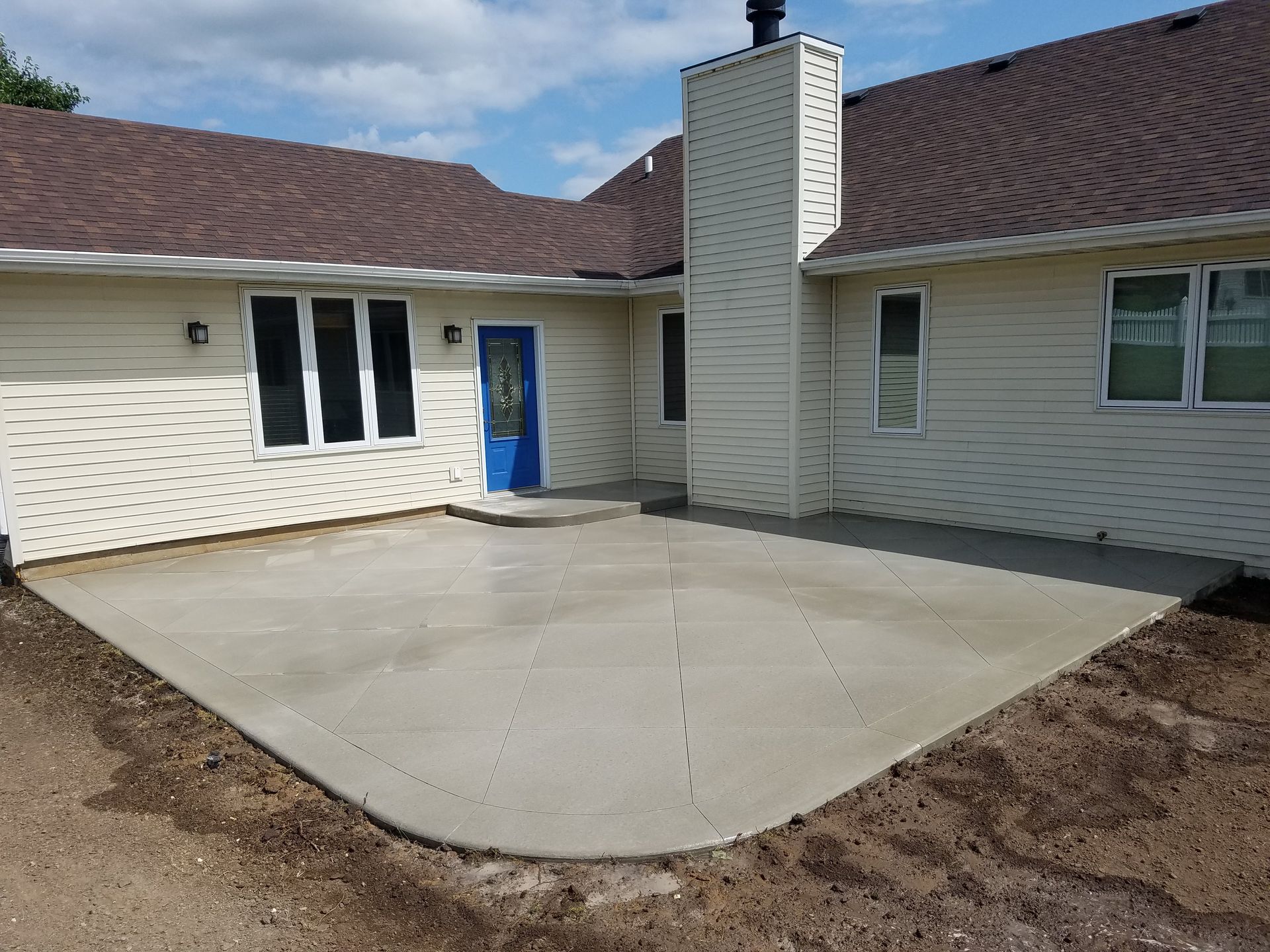 A white house with a blue door and a concrete patio in front of it.