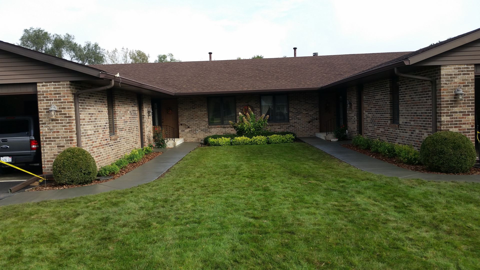 A brick house with a lush green lawn and a car parked in front of it.