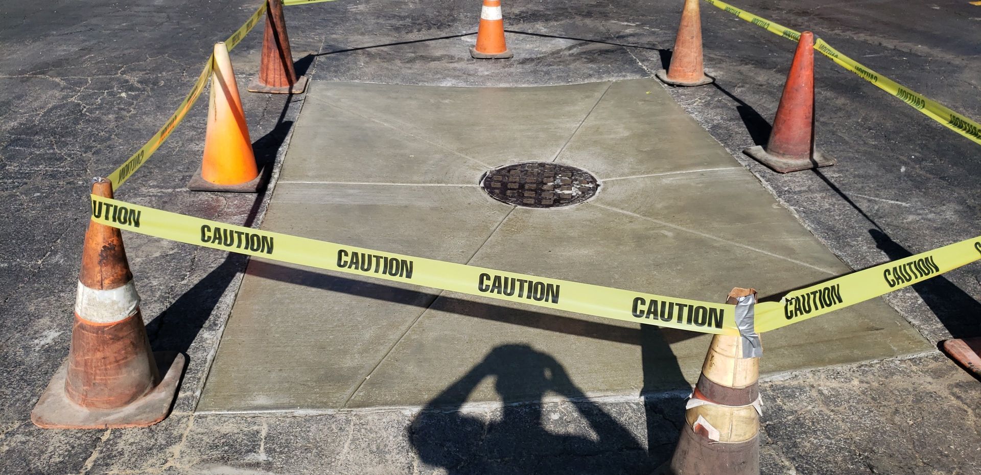 A manhole cover is surrounded by cones and caution tape.