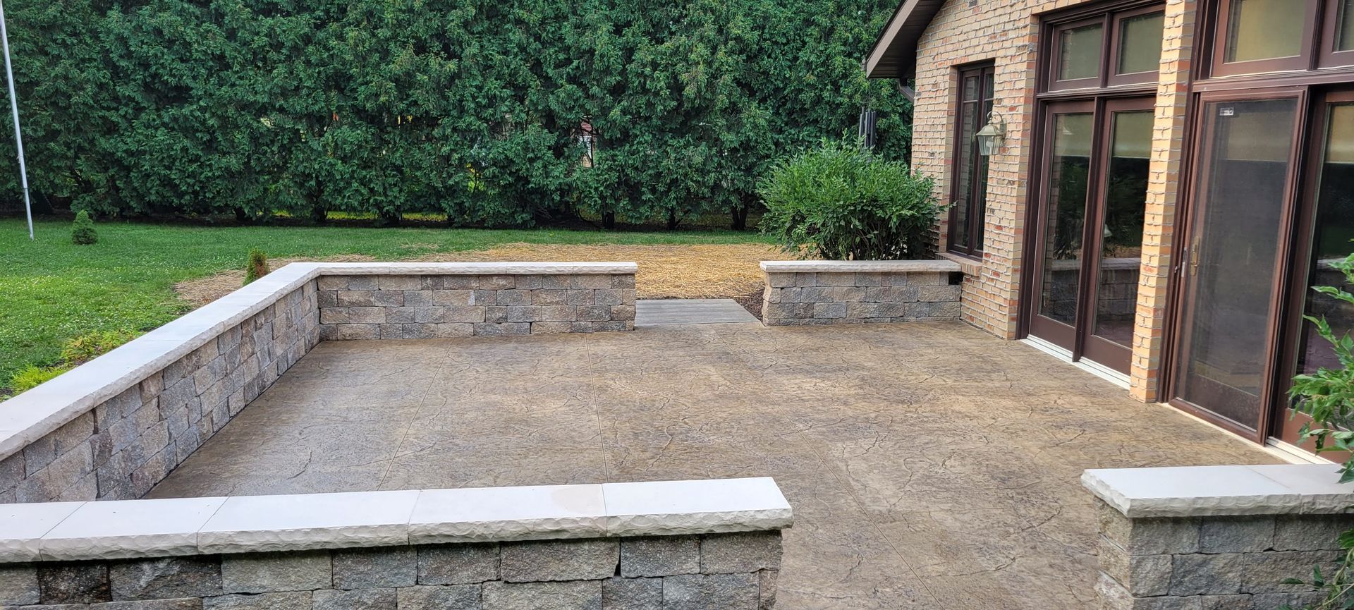 A patio with a stone wall and a brick building in the background.