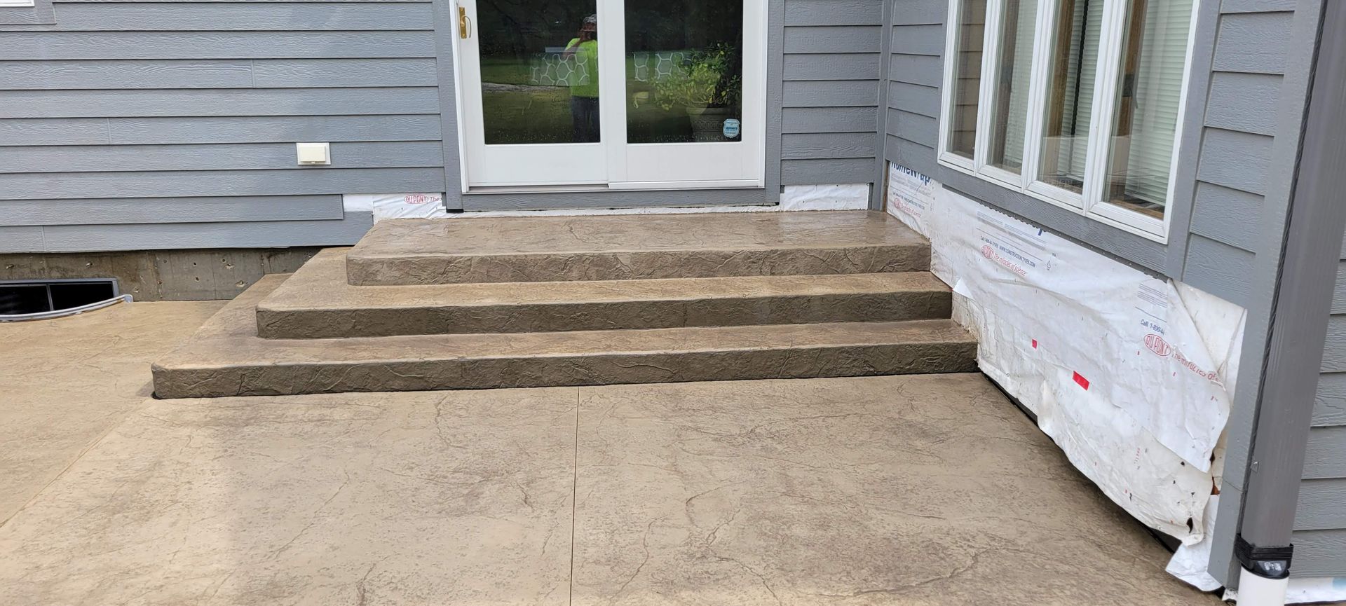 A concrete patio with stairs leading up to the front door of a house.