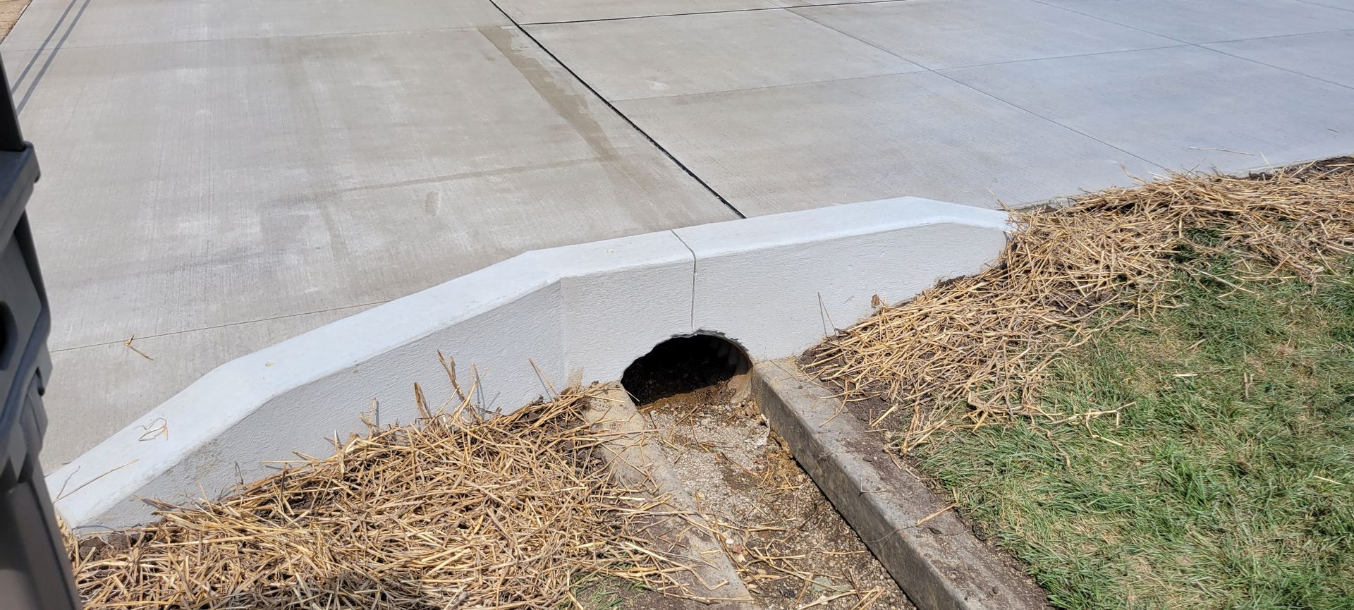A concrete curb with a hole in it next to a grassy area.