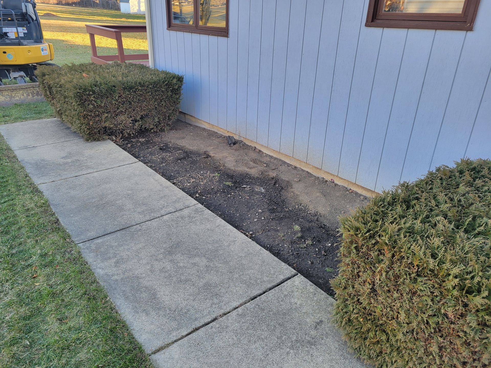 A sidewalk next to a house with a yellow excavator in the background.