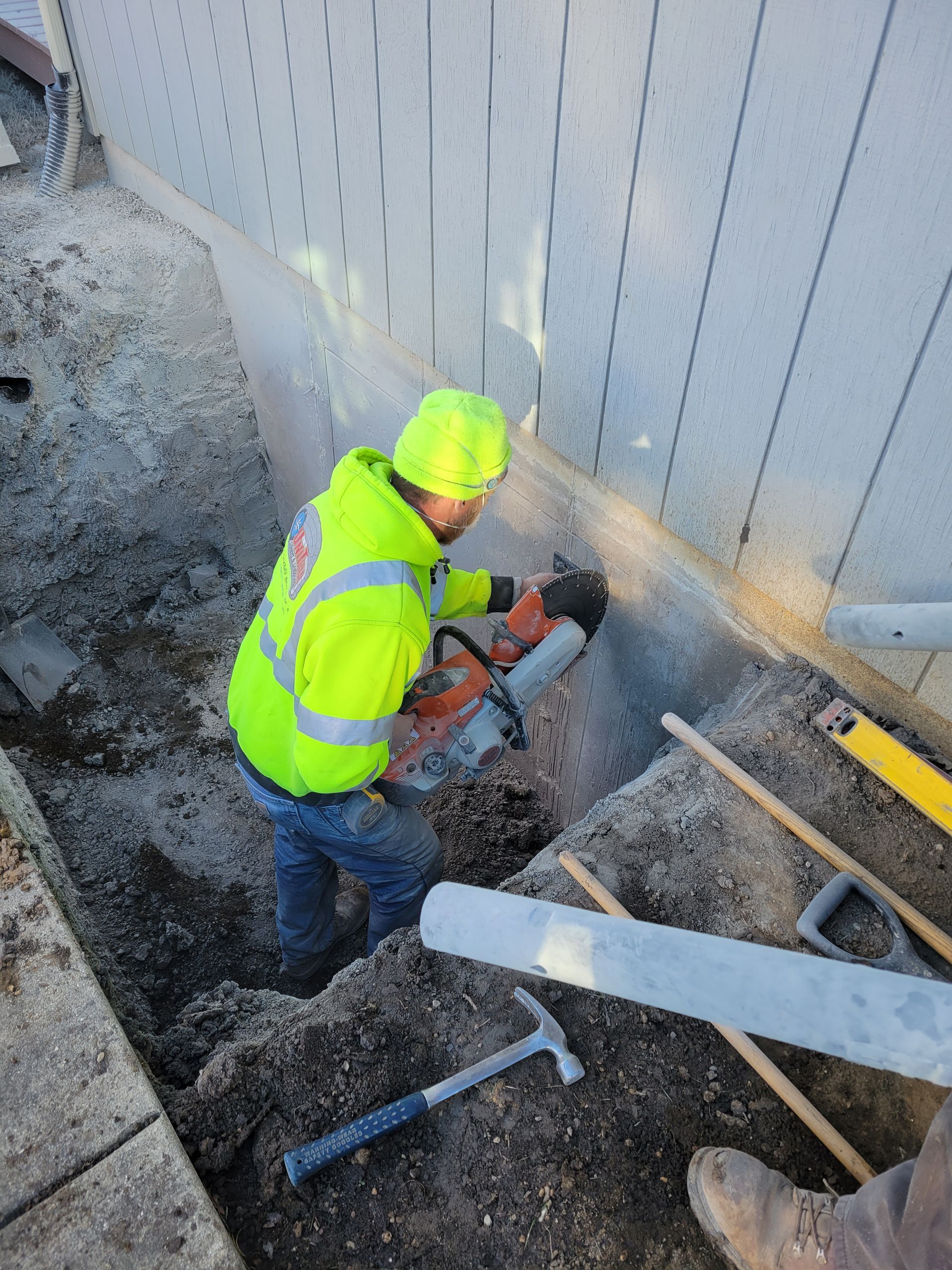 A man in a yellow jacket is cutting a pipe in the ground.