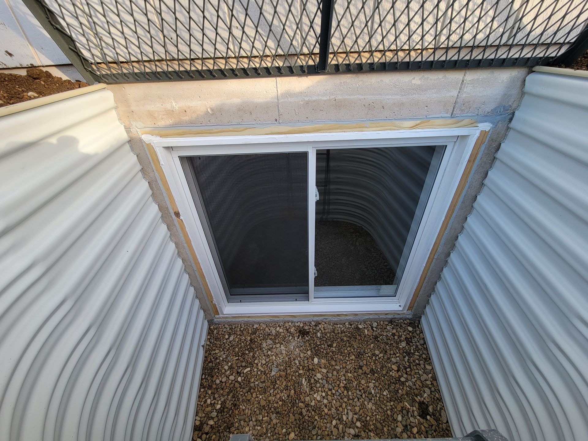 A window in a basement with a chain link fence around it.
