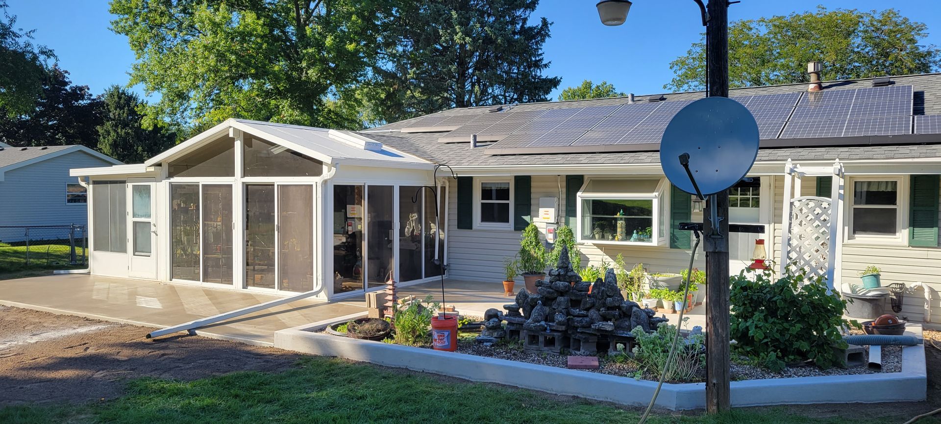 A white house with a screened in porch and a satellite dish in front of it.