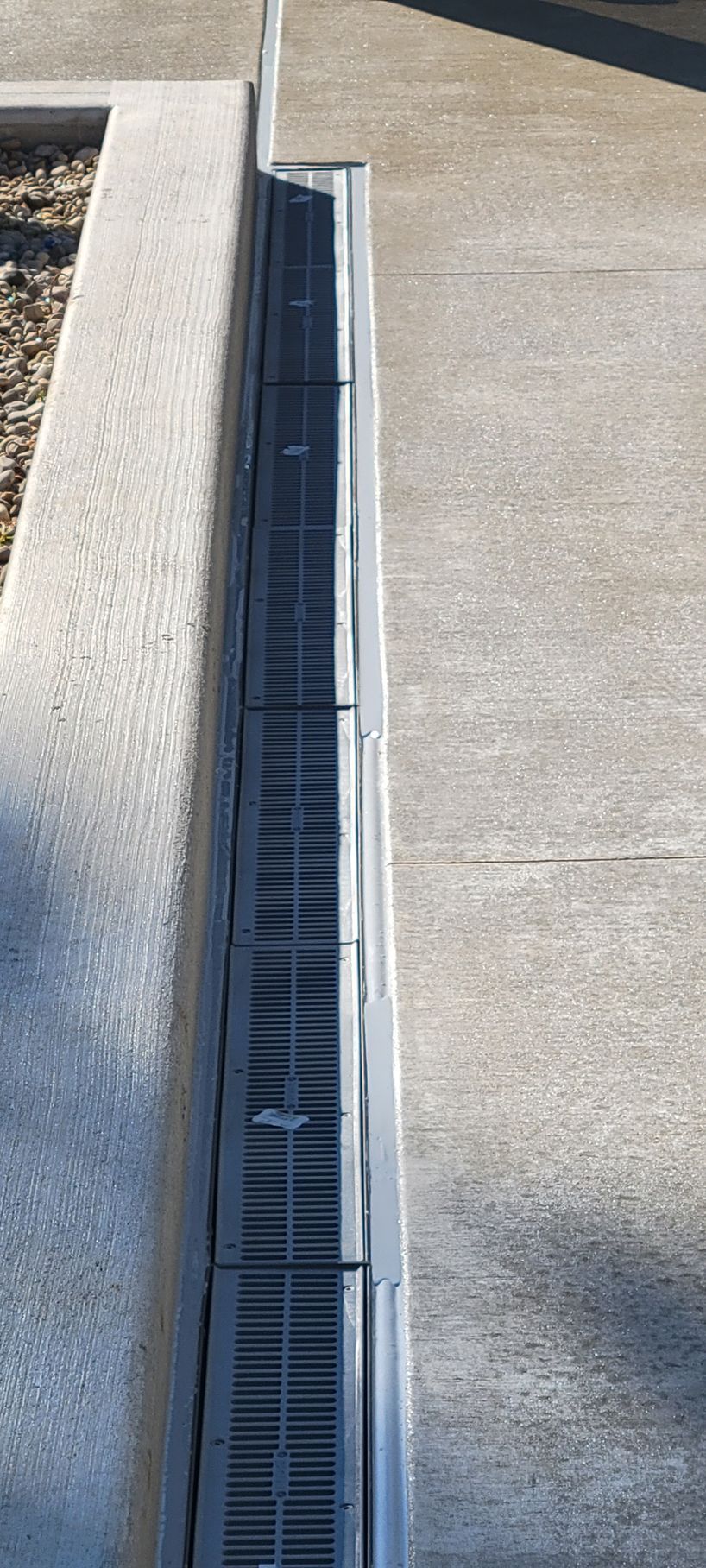 A close up of a drain on a sidewalk next to a wall.