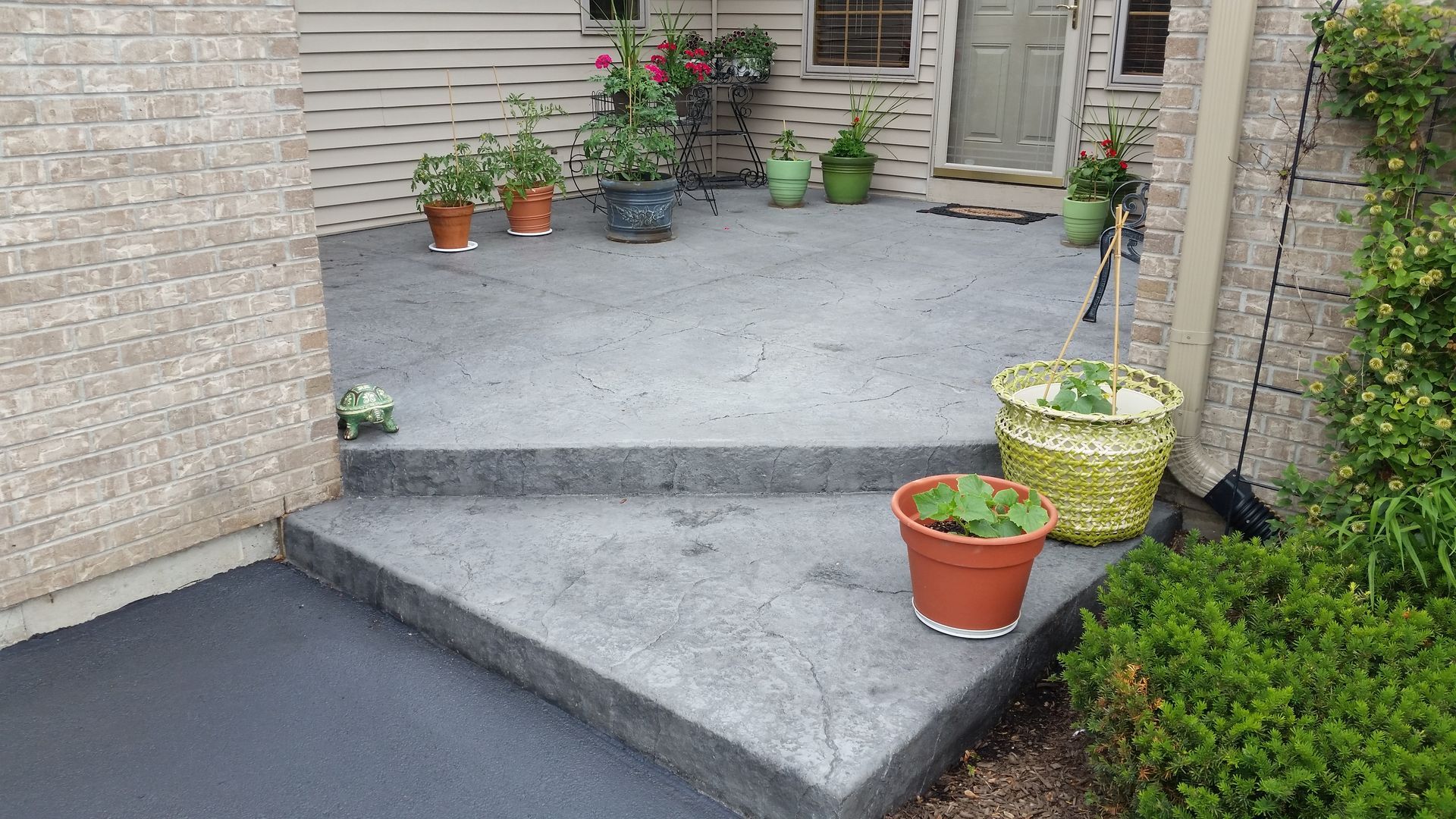 A concrete porch with potted plants in front of a brick house.