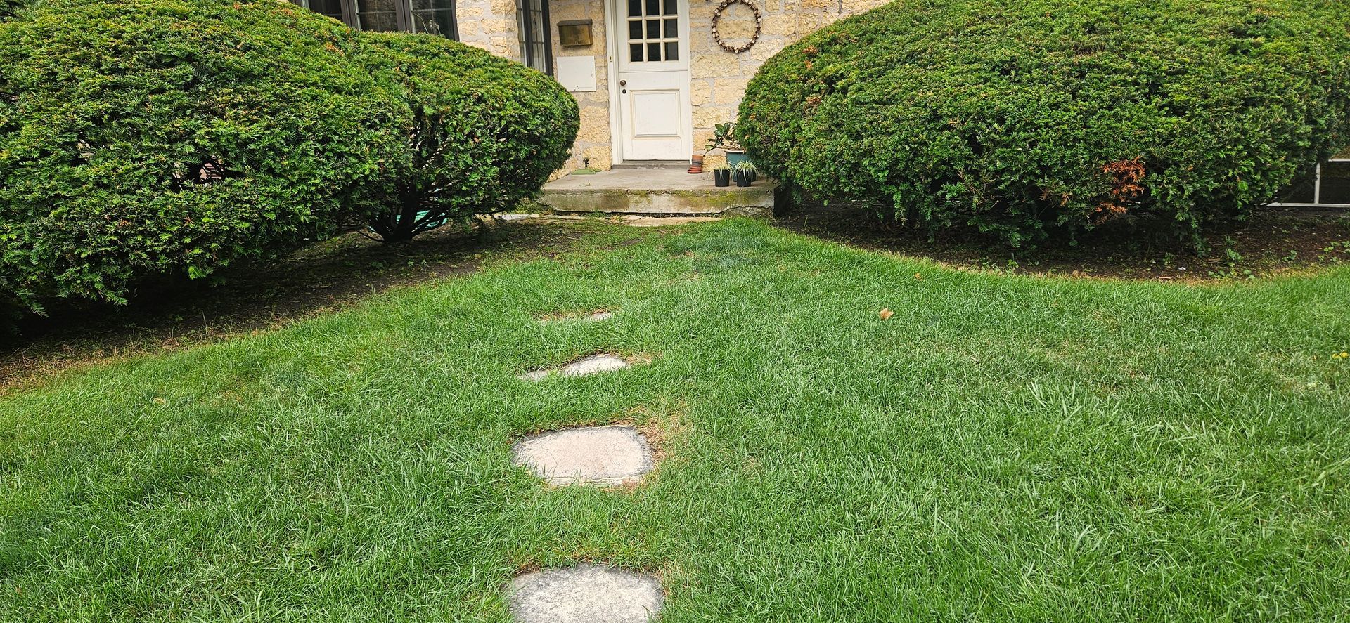 A lush green lawn with a stone walkway leading to the front door of a house.