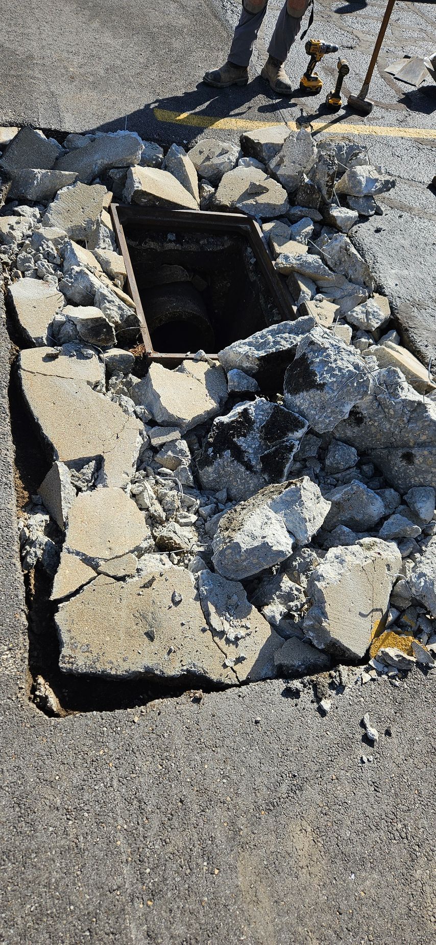 A manhole cover is being removed from the ground in a parking lot.