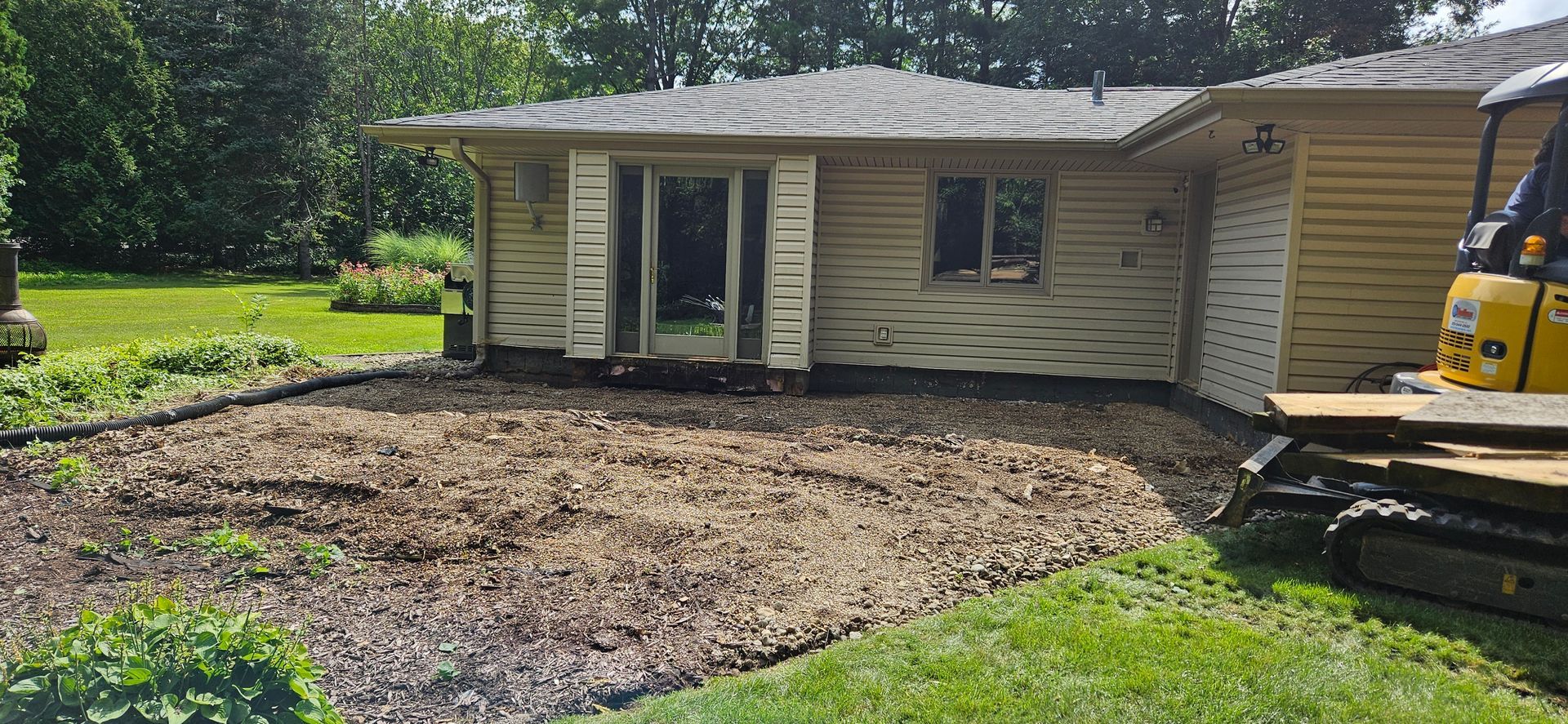 A house is being demolished and a yellow excavator is sitting in front of it.