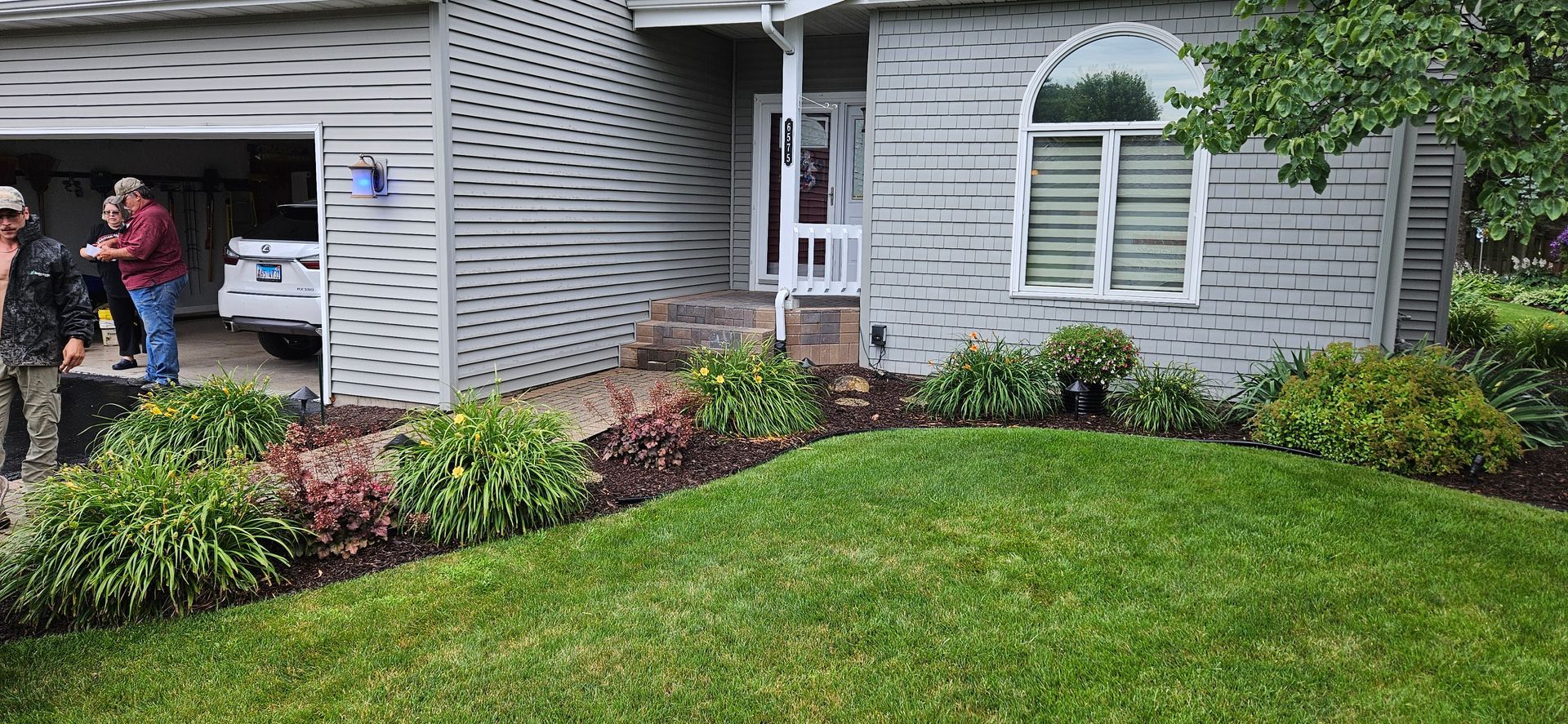A man is standing in front of a house with a lush green lawn.