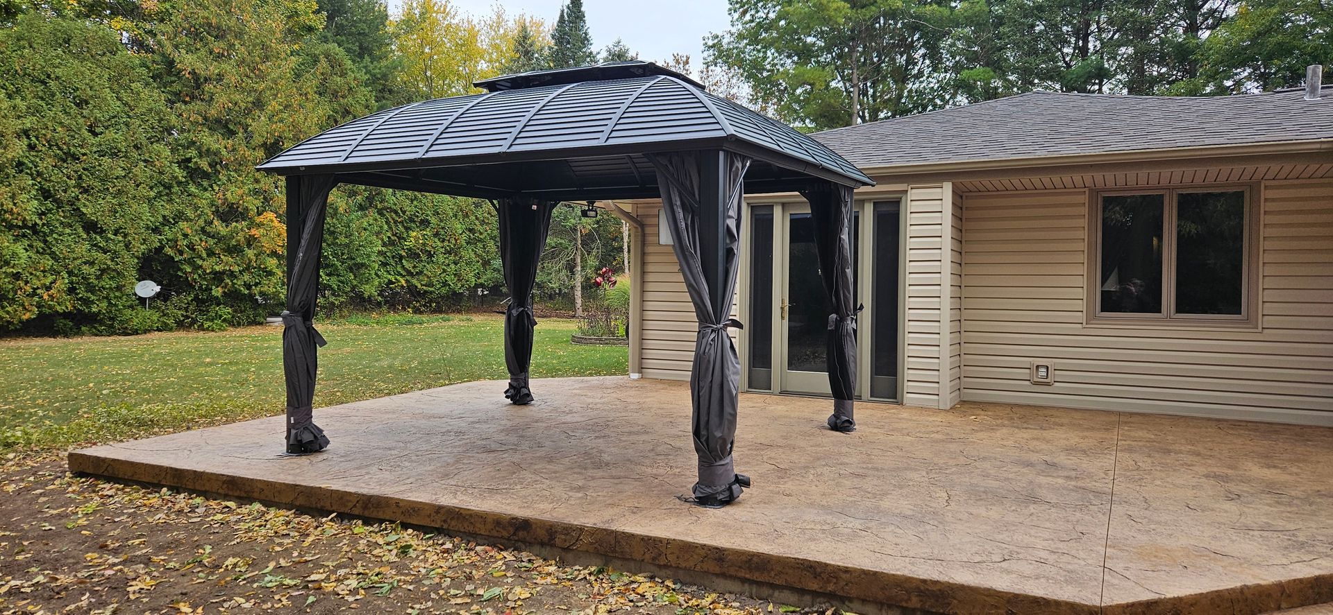 A gazebo is sitting on a patio in front of a house.