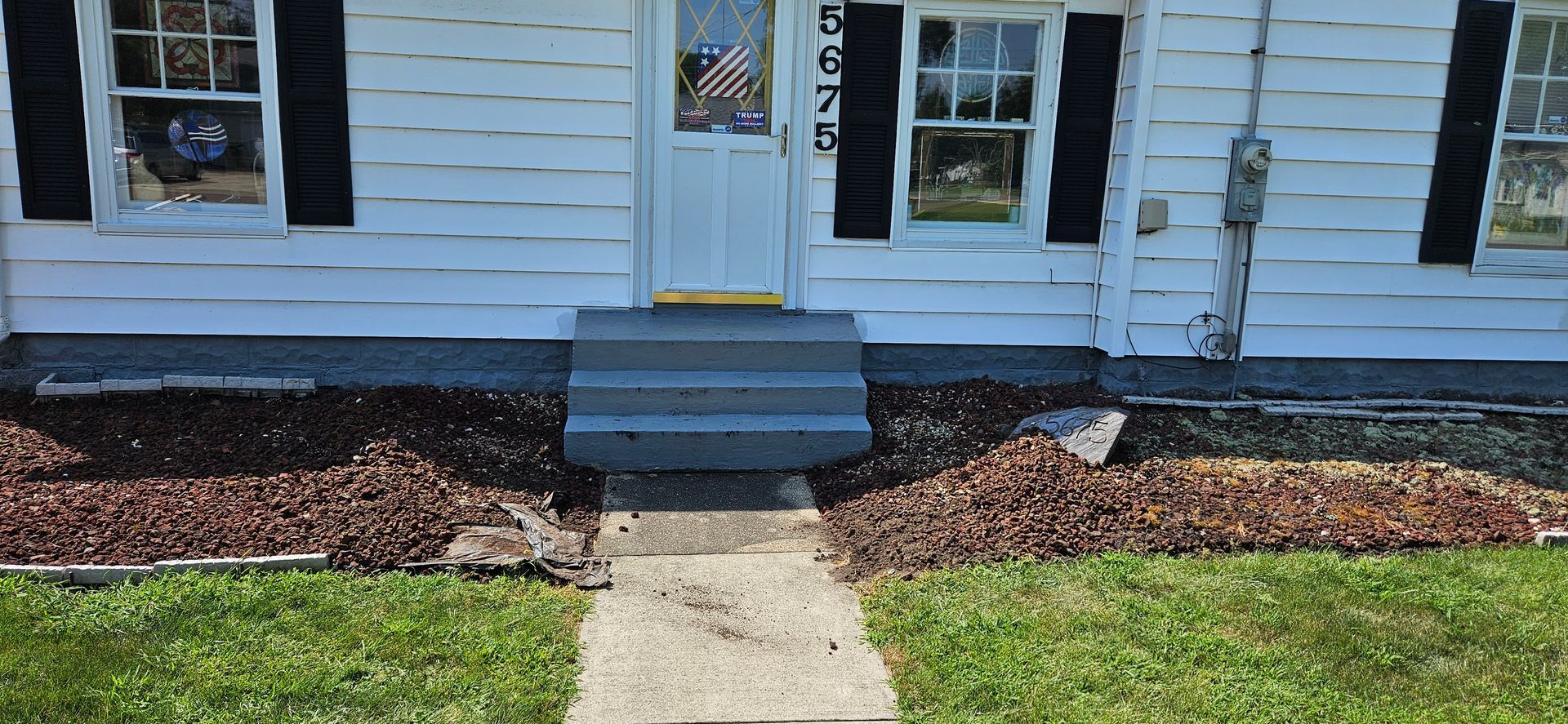 A white house with black shutters and a sidewalk in front of it.