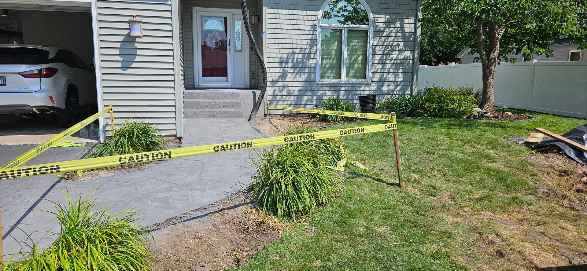 A car is parked in the driveway of a house surrounded by yellow tape.