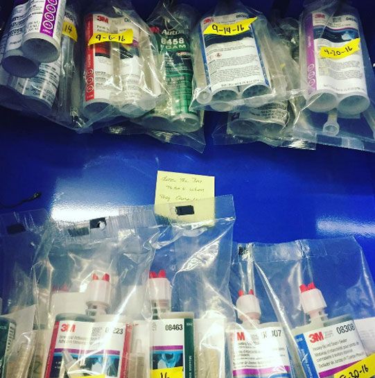 Bottles of 3m glue are lined up on a blue shelf