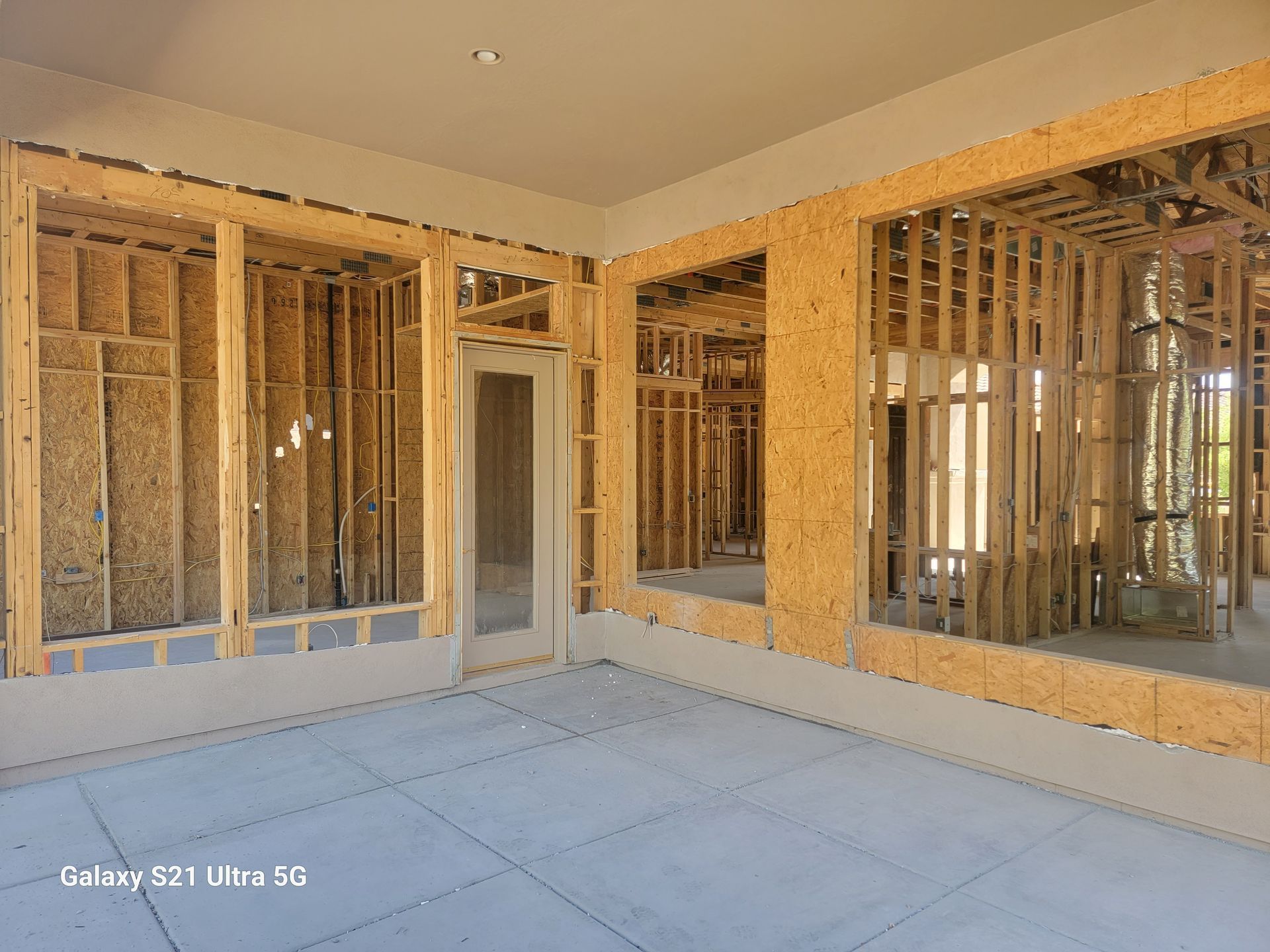 Interior of a room under construction, showing wooden frames for walls and windows, and a concrete floor.