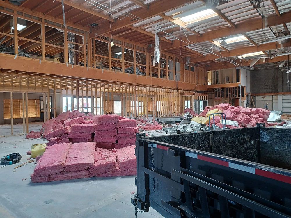Interior of a building under renovation, with exposed wooden frames, pink insulation, and a dumpster.