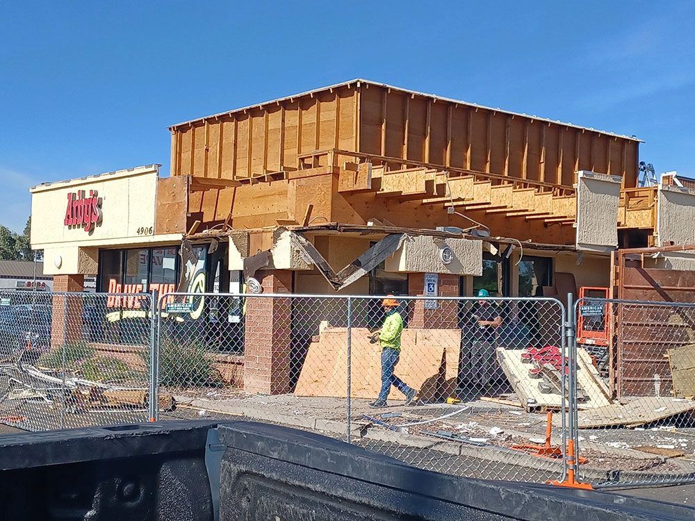 Building under construction; partially demolished exterior with exposed wood frame. A construction worker walks by.