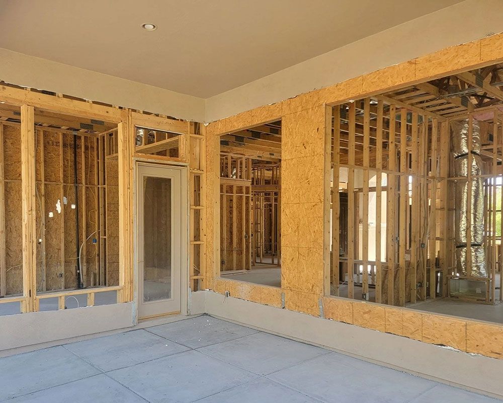Interior view of a building under construction, showing wooden framing for walls, windows, and a door.