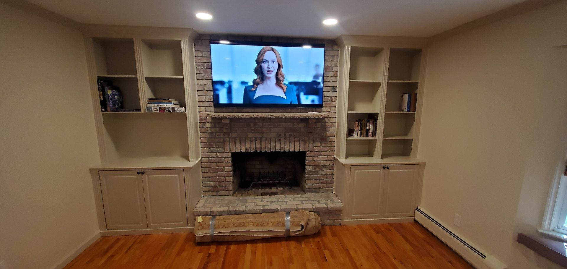 A living room with a fireplace and built-in shelves. TV mounted above the fireplace. Wooden floor.