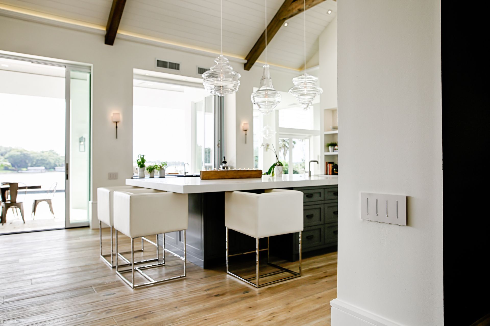 Modern kitchen with island, white stools, pendant lights, and sliding glass doors to a patio.